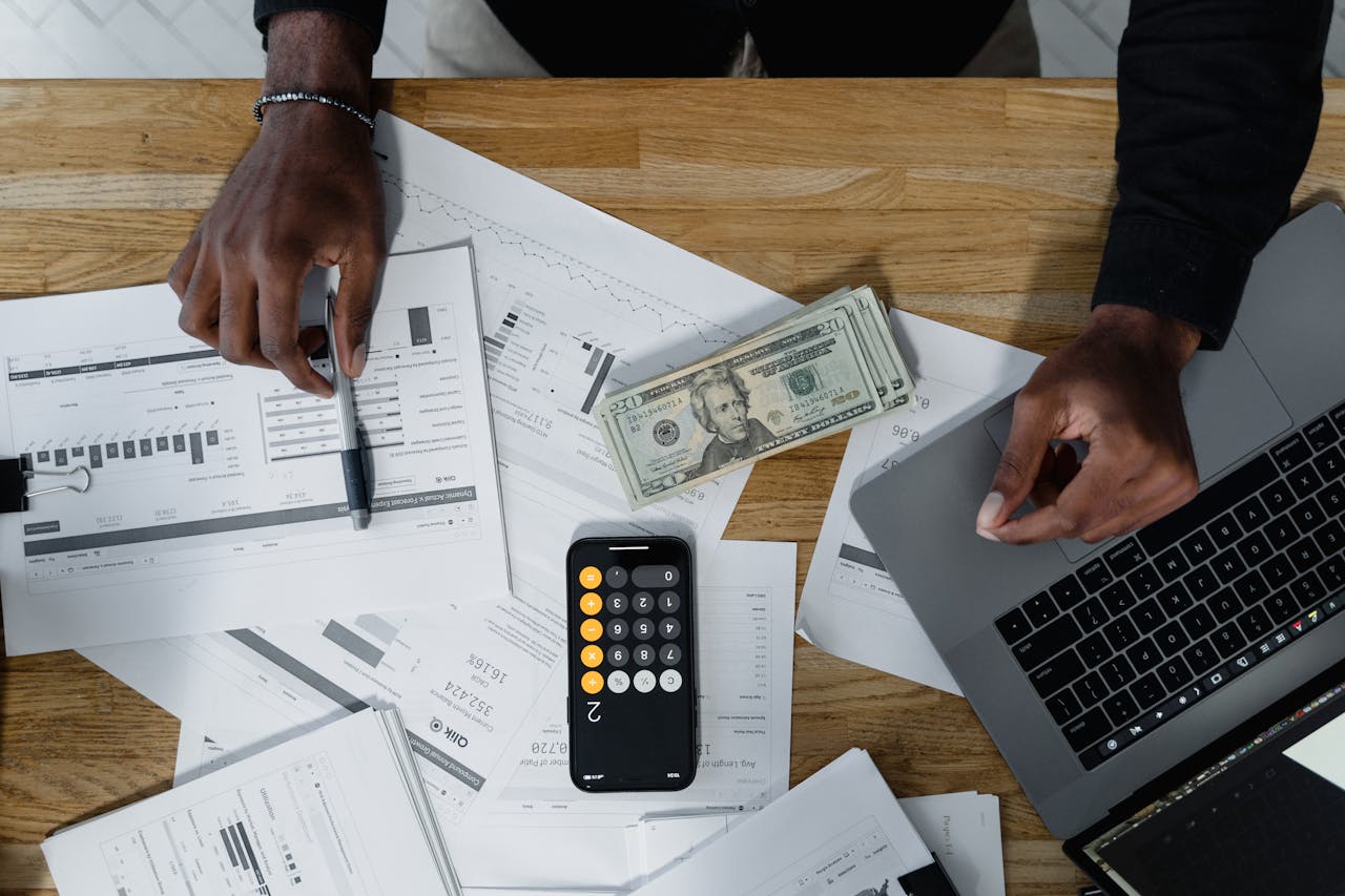 services-03 Hands calculate finances with papers, cash, and a laptop on a wooden desk.