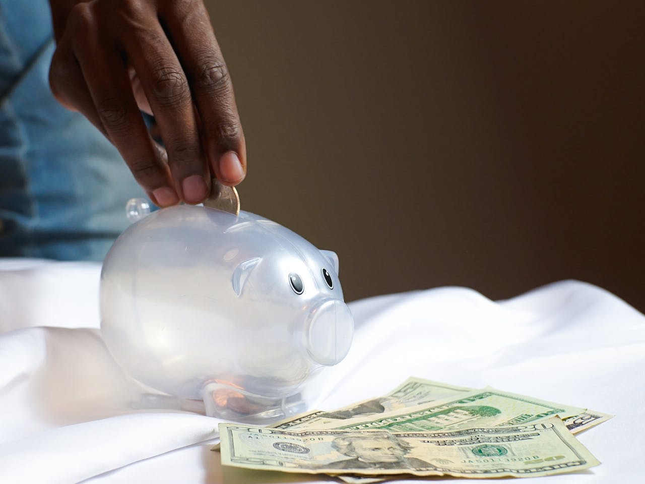 about-01 A hand placing a coin in a piggy bank with dollar bills nearby signifying savings and finance.