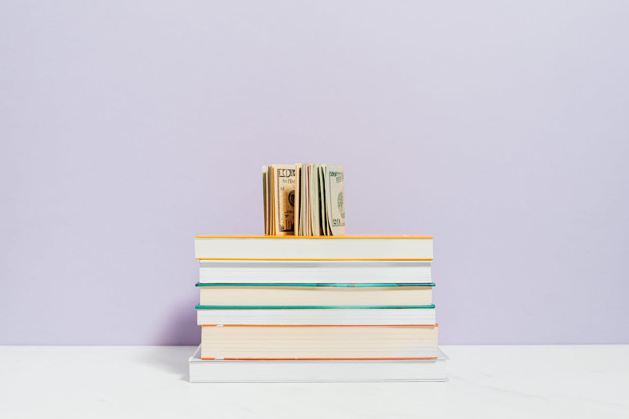 services-02 Stack of books with a stack of US dollar bills on top against a pastel background.